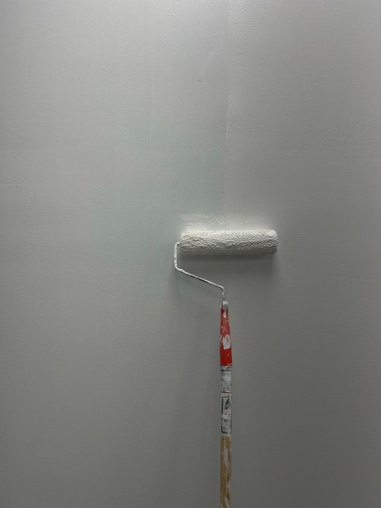 Malerarbeiten: Farbroller mit frischer weißer Farbe an einer glatten Wand